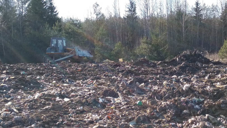 трактор убирает мусор на свалке